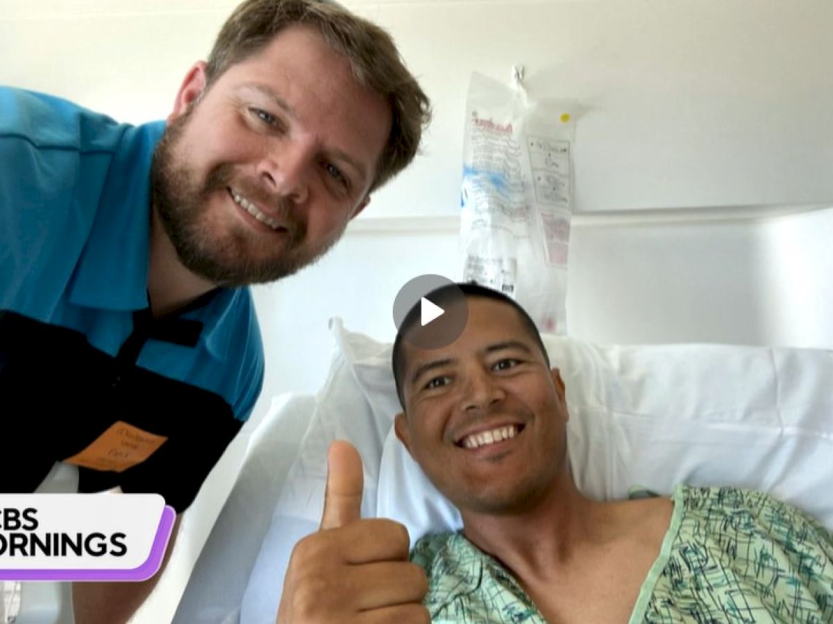 Two people are pictured; one is in hospital attire lying in a bed giving a thumbs-up, and the other person is smiling beside them.